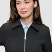 En person, der har en sort Essential Short Zip Jacket på over en lyseblå skjorte med krave.