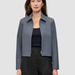 En kvinde har en Essential Short Zip Jacket i mørkegrå melange på over en sort top og bukser.