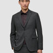 En mand iført en Motion Blazer Regular i farven Pepper Grey over en mørk skjorte med knapper.