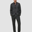 En mand har en Motion Blazer Regular i farven Pepper Grey på over en mørk skjorte med knapper og loafers.