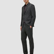 En mand iført en Motion Blazer Slim i farven Pepper Grey og matchende bukser over en mørk skjorte med knapper og loafers.