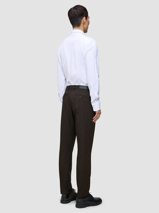 En person set bagfra, iført en hvid skjorte, Motion Suit-bukser i Regular-pasform i farven Cognac og sorte dressko.