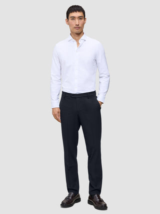 En mand iført en hvid skjorte med knapper, Motion Suit-bukser i regular-pasform i midnatsblå og læderloafers.