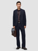 En mand iført et par marineblå Motion Suit-bukser i afslappet pasform Midnight Blue, en mørk skjorte og loafers holder en brun lædermappe.