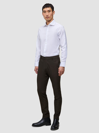 En mand iført en hvid skjorte med knapper, Motion Suit Pants Slim Cognac og sorte støvler.