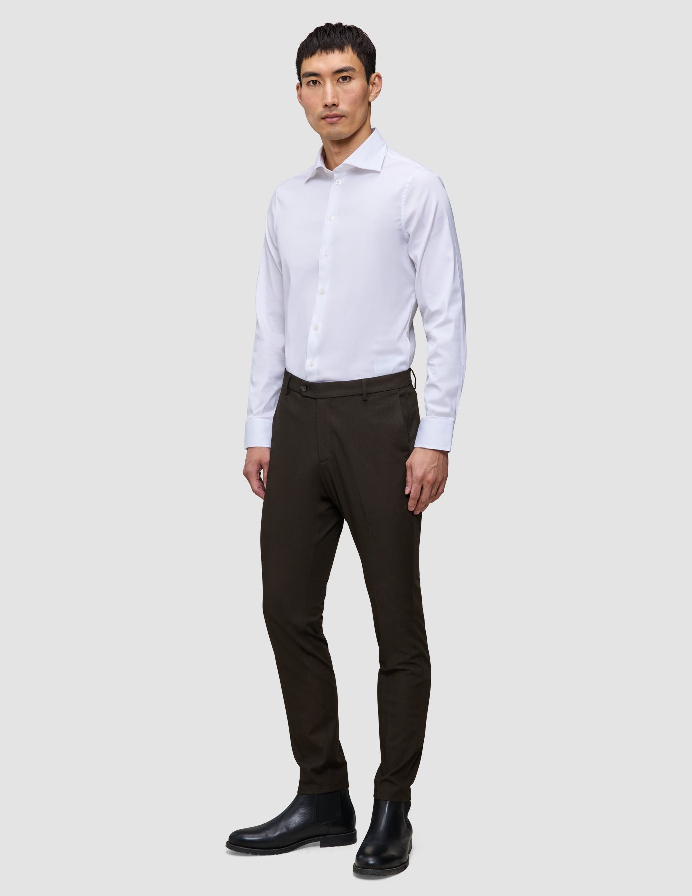 En mand iført en hvid skjorte med knapper, Motion Suit Pants Slim Cognac og sorte støvler.