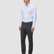 En mand iført en hvid skjorte med knapper, Motion Suit-bukser i Slim-pasform i farven Pepper Grey og sorte lædersko.