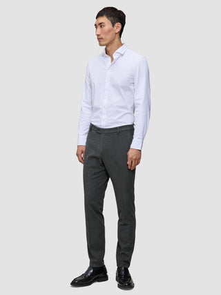 En mand iført en hvid skjorte med knapper, Motion Suit-bukser i Slim-pasform i farven Pepper Grey og sorte lædersko.
