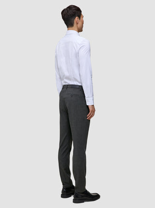 En mand i en hvid skjorte med knapper og grå Motion Suit-bukser i farven Slim Pepper Grey står med ryggen til kameraet.