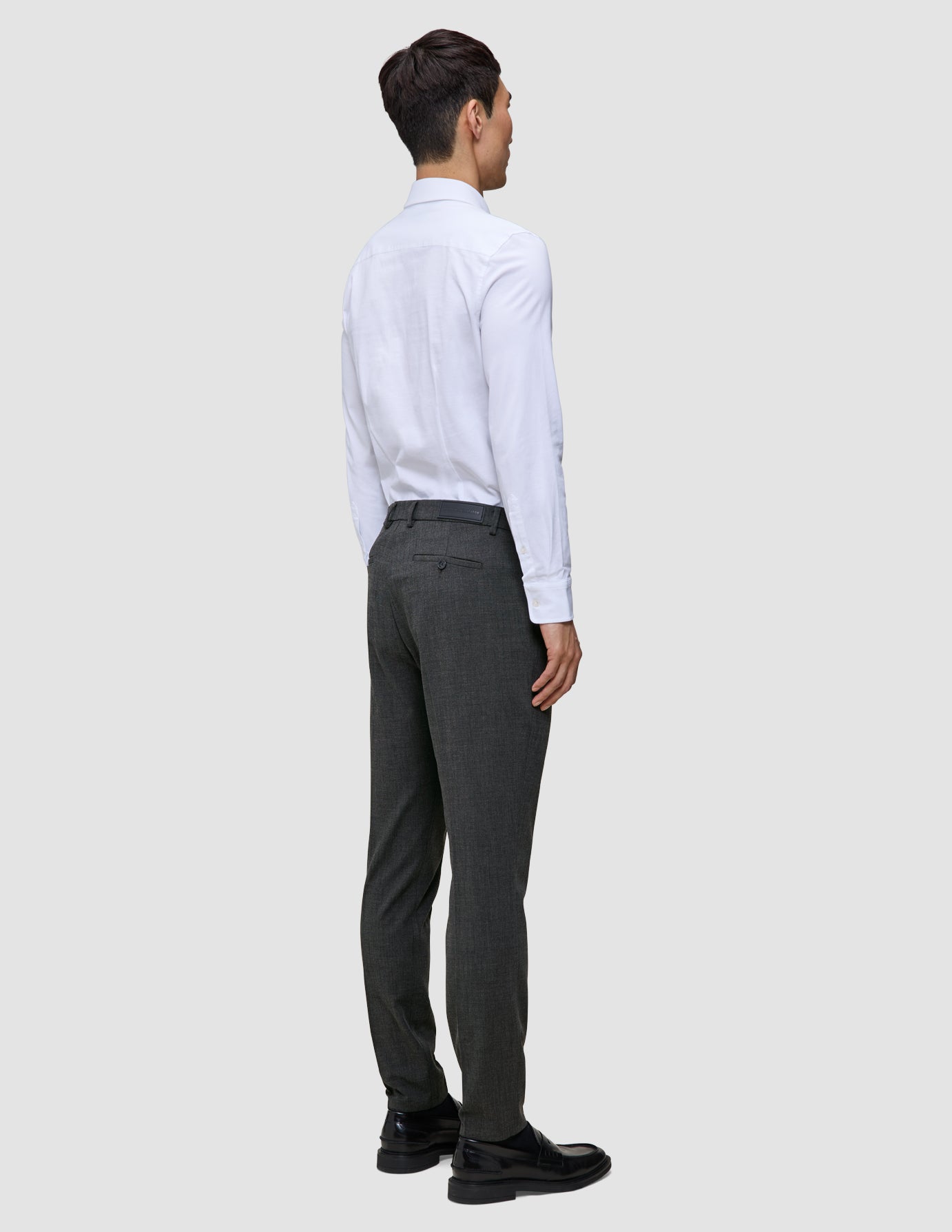 En mand i en hvid skjorte med knapper og grå Motion Suit-bukser i farven Slim Pepper Grey står med ryggen til kameraet.