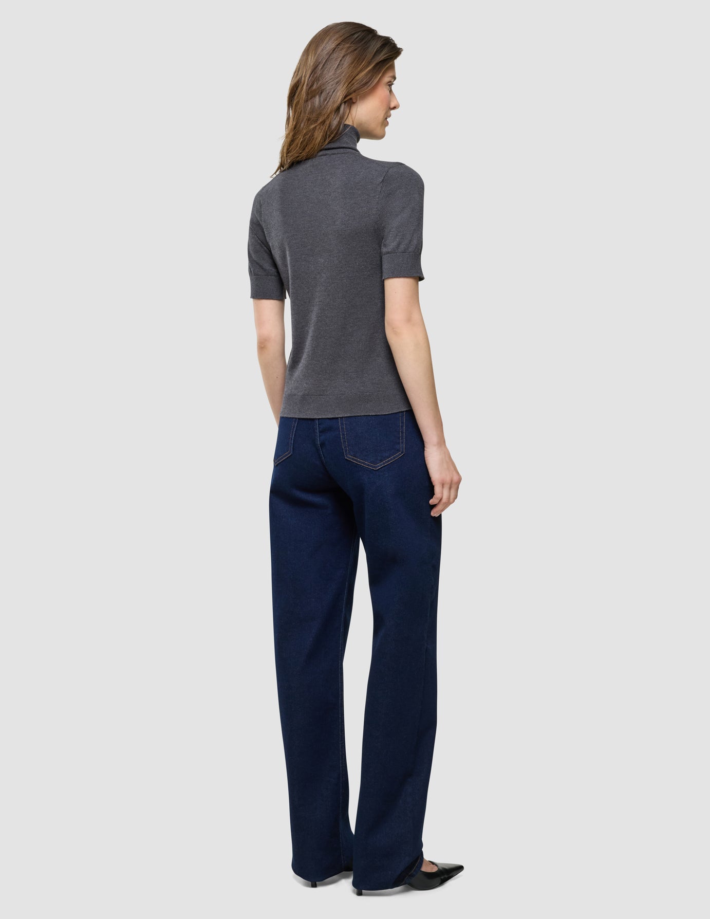 Quinn Turtleneck Short Sleeved i Cool Brown, helfigur bagfra, kvinde i grå trøje og mørkeblå bukser.