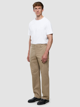 En mand iført en hvid T-shirt, Refine Cotton Pants i sandfarve med afslappet pasform og sorte dressko.
