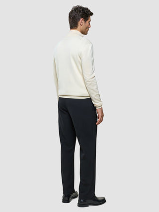 En mand set bagfra, iført en Seamless Core Knit Half Zip Birchwood, mørke bukser og sorte loafers.