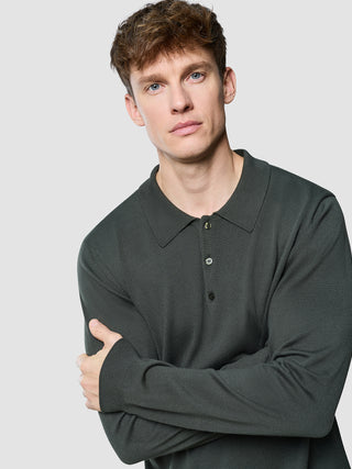En mand med armene over kors, iført en Seamless Core Knit langærmet polo i farven Green Night.