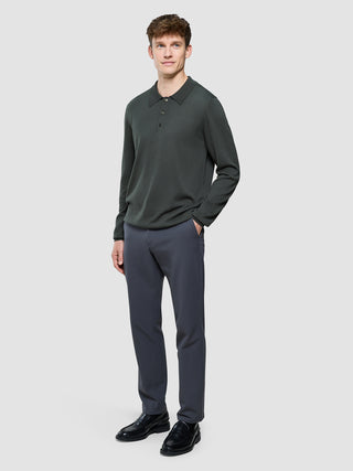 En mand iført en Seamless Core Knit langærmet polo i farven Green Night og grå bukser.