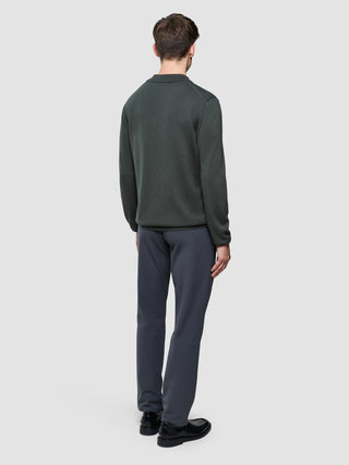 En mand set bagfra, iført en Seamless Core Knit langærmet polo i farven Green Night og grå bukser.
