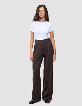 En person iført en hvid T-shirt og et par Serene Pants Wide Walnut Herringbone, som er mørkebrune bukser med brede ben og herringbone-mønster.