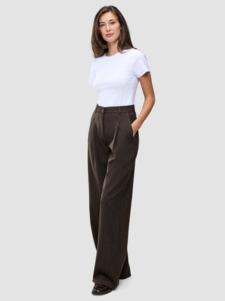En kvinde iført en hvid T-shirt og et par Serene Pants Wide Walnut Herringbone-bukser med høj talje og brede ben i nålestribet mønster.