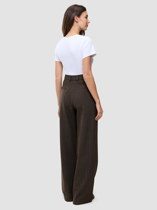 En person set bagfra, iført en hvid T-shirt og mørkebrune Serene Pants Wide Walnut Herringbone-bukser med høj talje og brede ben.
