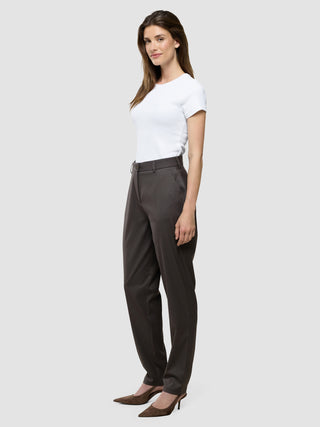 En kvinde set i profil iført en hvid T-shirt, Women Skye Pants Tapered Dark Chestnut Melange og højhælede sko med spids snude.