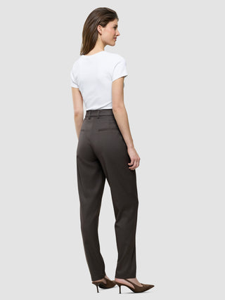 En kvinde set bagfra, iført en hvid T-shirt, Women Skye Pants Tapered Dark Chestnut Melange og højhælede sko med spids tå.