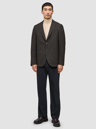 En mand iført et look bestående af strik og blazer med en beige sweater, en mørk mønstret blazer, mørke bukser og loafers.