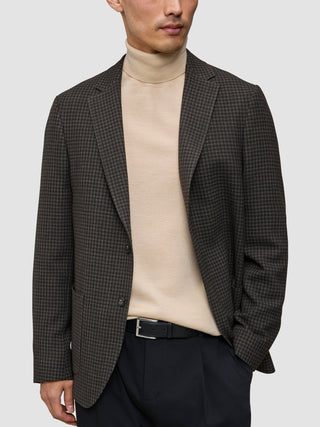 En mand iført et look bestående af strik og blazer med en mønstret uldblazer, mørke bukser og et sort bælte.