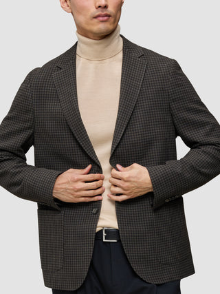 En person iført et look bestående af strik og blazer, med en merino-trøje med rund hals under en mørk, mønstret uldblazer.