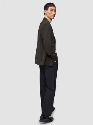 En mand i et look med strik og blazer, iført en Premium Merino-trøje med rund hals, en mørk uldblazer med mønster og mørke bukser.