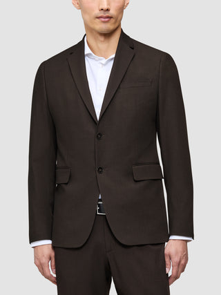 En mand iført en mørkebrun The suit that does it all-jakke over en eksklusiv hvid skjorte med krave.