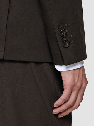 Nærbillede af en mørkebrun jakke fra The Suit That Does It All med fire knapper på ærmet, båret over en Elevated-skjorte.