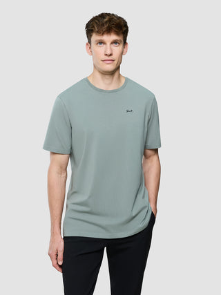 En mand iført en Supima Legacy-T-shirt i farven »Mist Green« med »Snt.« broderet på brystet.