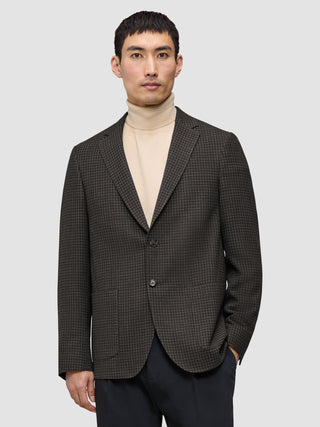 En mand iført en mørkebrun, slim-fit Timeless Wool Blazer med tern over en beige rullekravebluse.