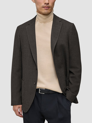 En mand har en mørkebrun, slim-fit Timeless-uldblazer med tern på over en beige rullekravesweater og sorte bukser.