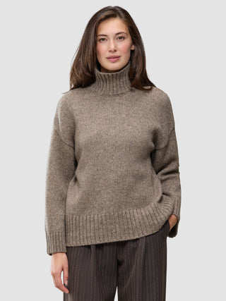 En kvinde iført en Women Chunky Soft Wool Knit Turtleneck Taupe Melange – en grovstrikket merinoullstrøje i taupe-melange.