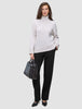 En kvinde i en beige rullekravesweater og et par sorte Women GO2-bukser med høj talje i lige snit, der holder en sort håndtaske.