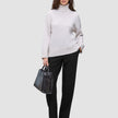 En kvinde i en beige rullekravesweater og et par sorte Women GO2-bukser med høj talje i lige snit, der holder en sort håndtaske.