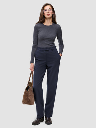 En kvinde i en grå langærmet bluse har Women GO2 Pants Straight Blue Nights på og holder en brun håndtaske.