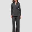 En kvinde er klædt i en koksgrå Women Nara Blazer Fitted Black Check og bukser med brede ben, der er et udtryk for elegant dansk design.