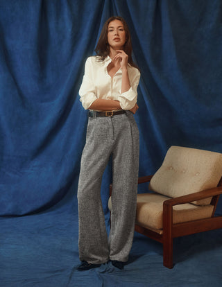 En kvinde har en hvid Women’s Oxford Shirt White Orchid Slim på, som er stukket ned i et par grå bukser med brede ben.