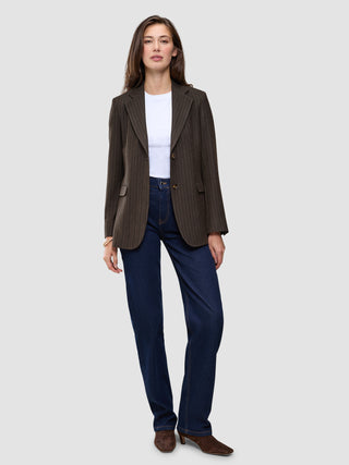 En person iført en Women Serene Blazer Regular Walnut Herringbone over en hvid T-shirt, mørkeblå jeans og brune ankelstøvler.