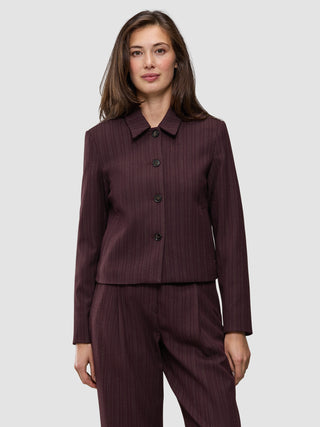 En kvinde bærer en Women Serene Short Jacket Berry Pinstripe i et mørkt bærfarvet stof med fine striber, der afspejler klassisk dansk design.