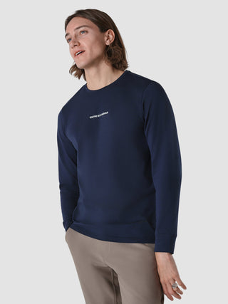 En mand har en marineblå Supima Autograph langærmet T-shirt på med teksten »SHAPING NEW TOMORROW« trykt på brystet.