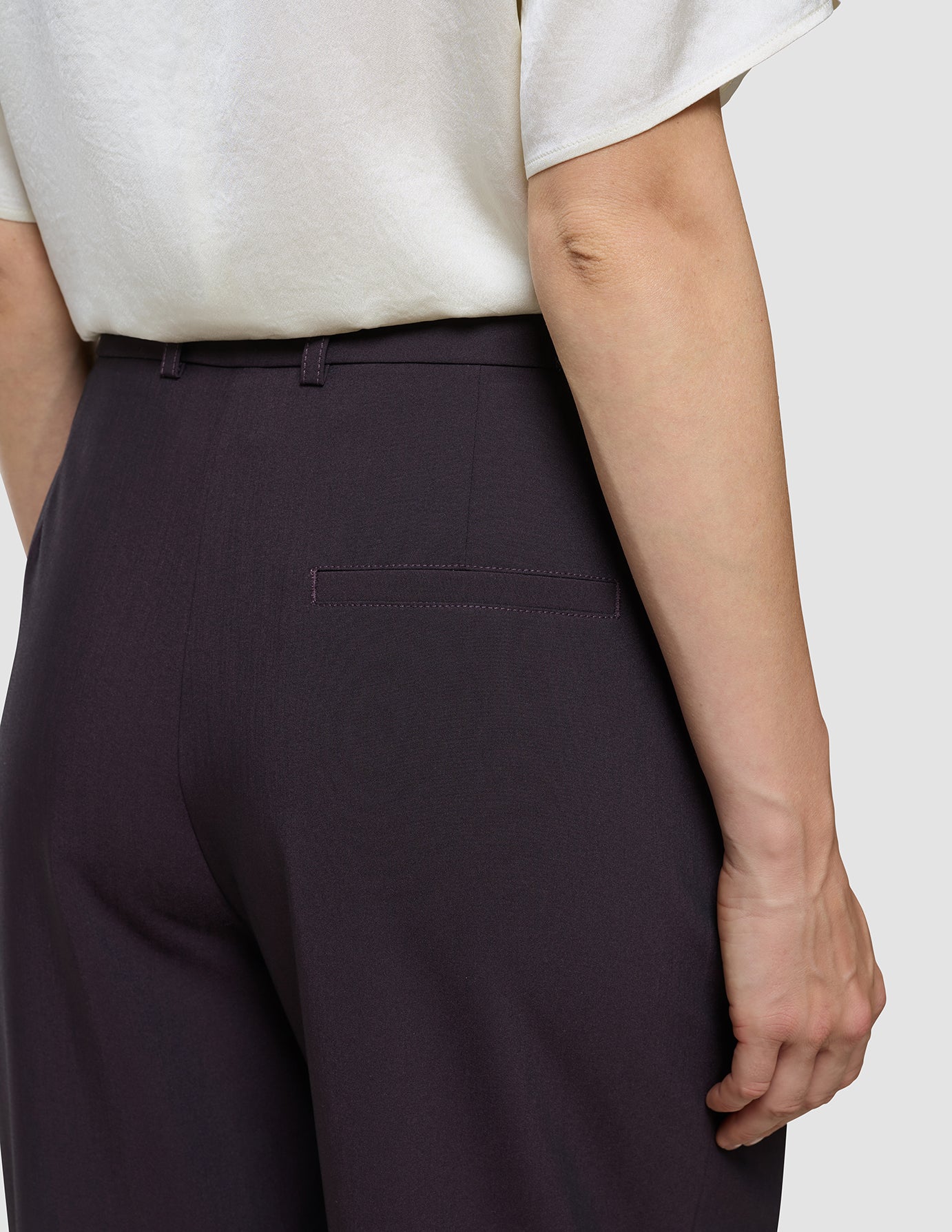 En person iført en hvid bluse og et par Avira-bukser til kvinder i modellen »Wide« i farven »Burgundy Berry« med en detalje på baglommen.
