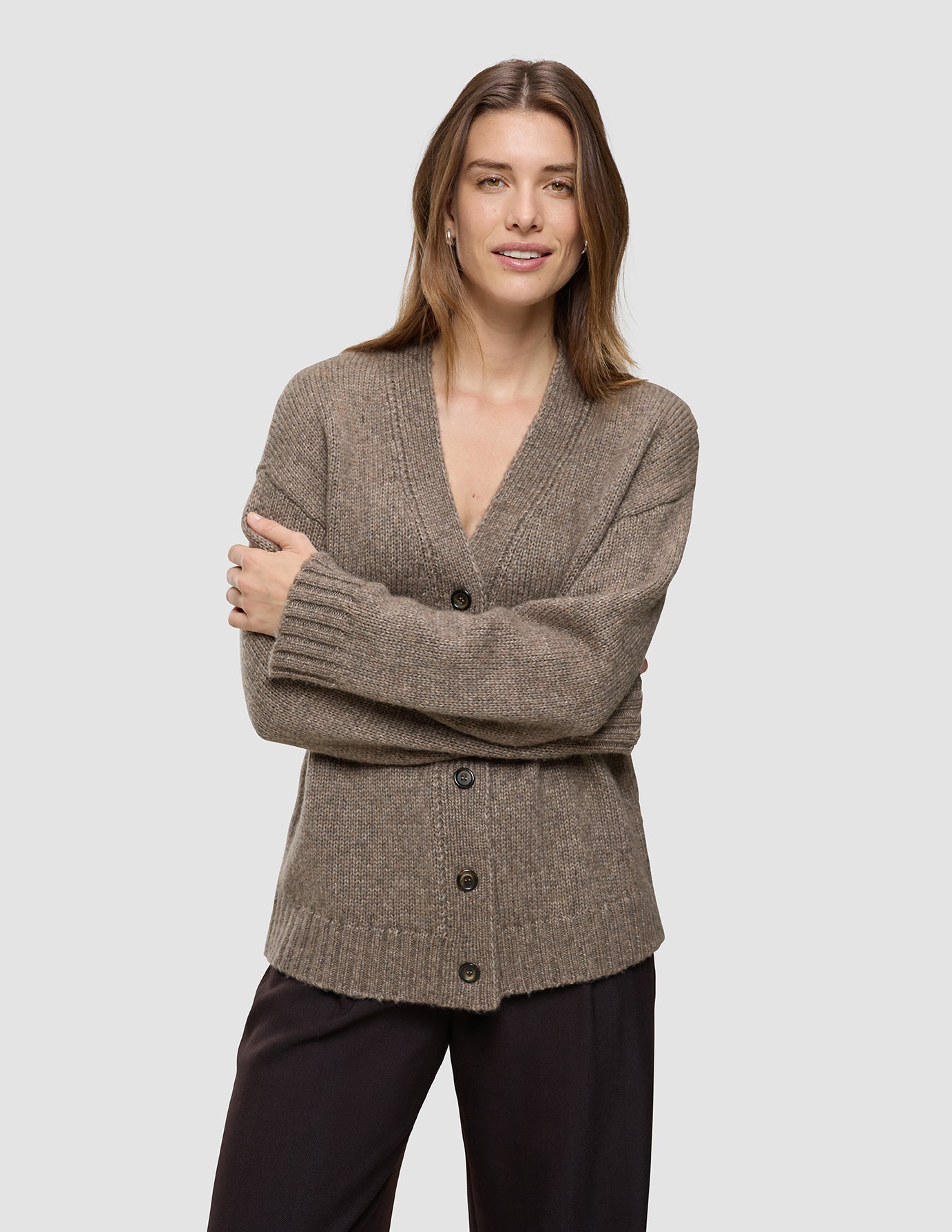 En person iført en Women’s Chunky Soft Wool Knit Cardigan Taupe Melange, en taupefarvet, grovstrikket cardigan med V-udskæring.