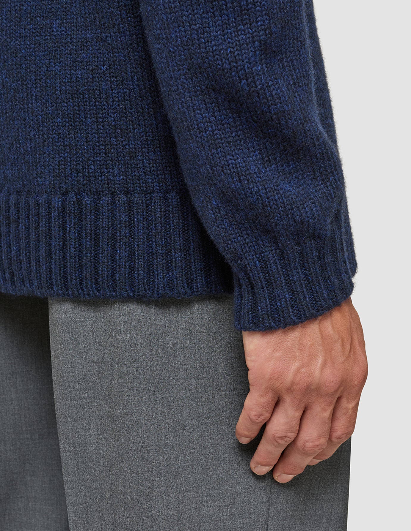Nærbillede af en tyk, blød uldstrikket sweater i mørk marineblå melange med rund hals, ribkant ved ærmerne og forneden.