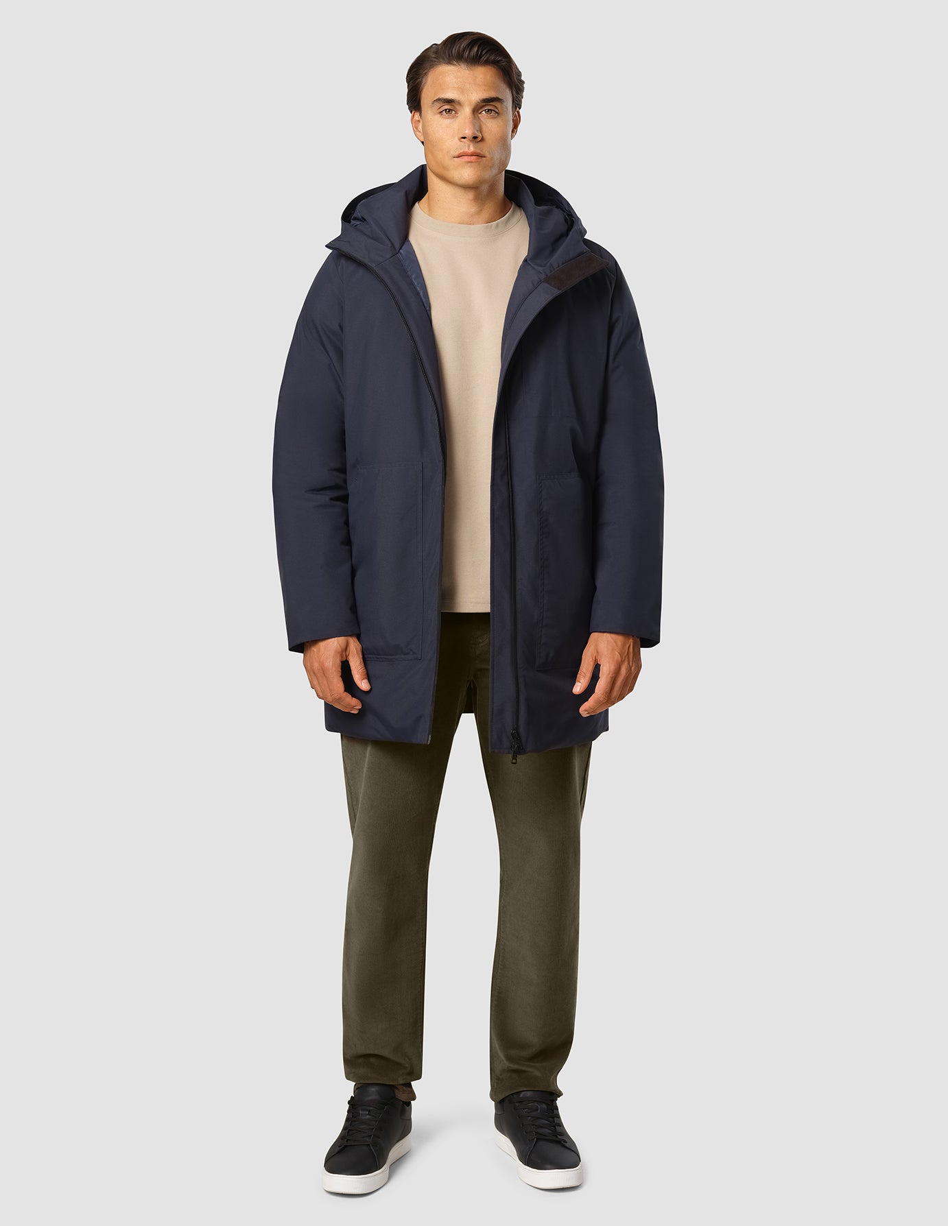 En mand iført en mørkeblå Utility-jakke over en beige sweater og mørke bukser.