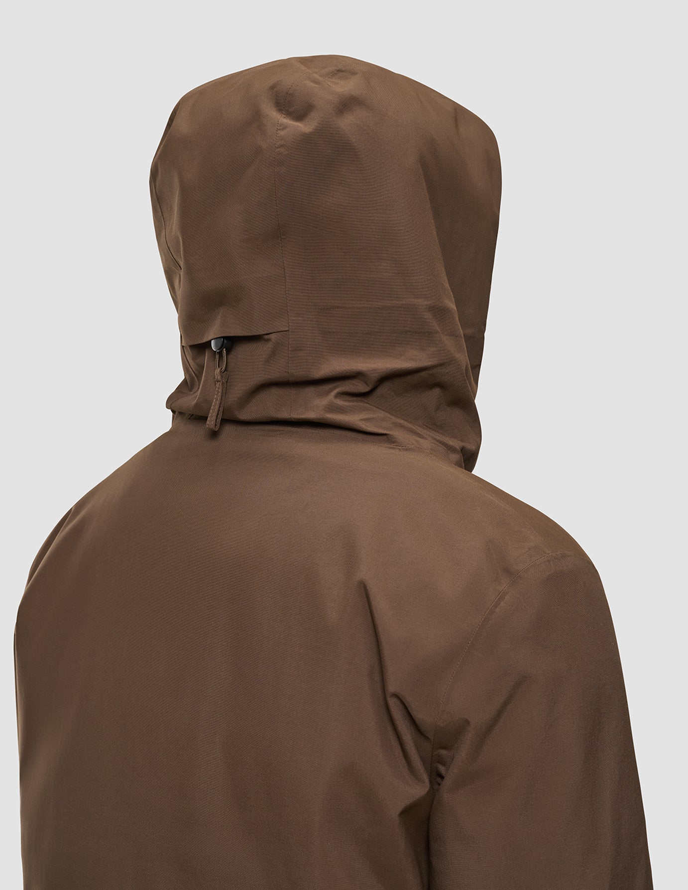 Bagfra-billede af en person, der bærer en Utility Jacket Saddle Brown med hætte, fremstillet af genanvendt polyester.