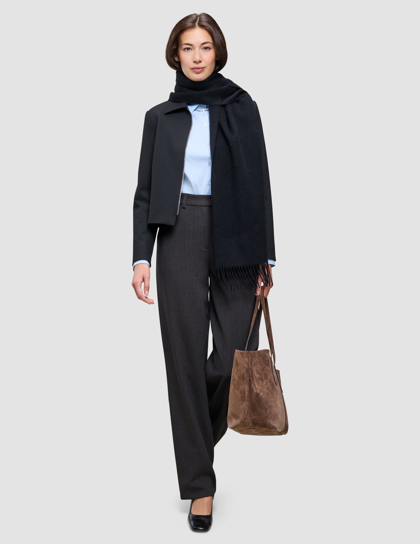 En kvinde iført en lyseblå Oxford-skjorte, bukser og et tørklæde – et nemt look til kontoret – og med en brun totebag i hånden.