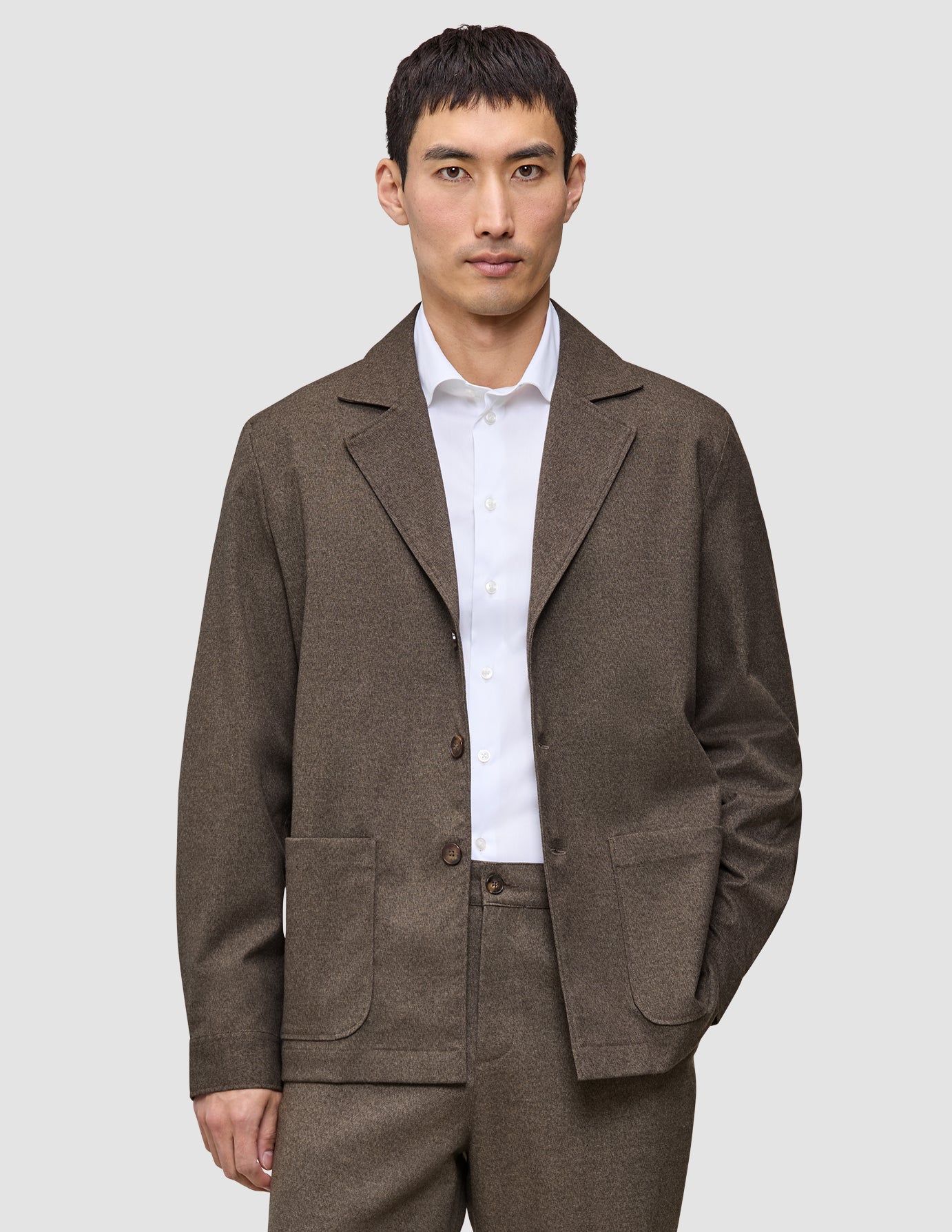 En mand iført en brun Atelier Overshirt Dark Beige over en hvid skjorte med knapper.